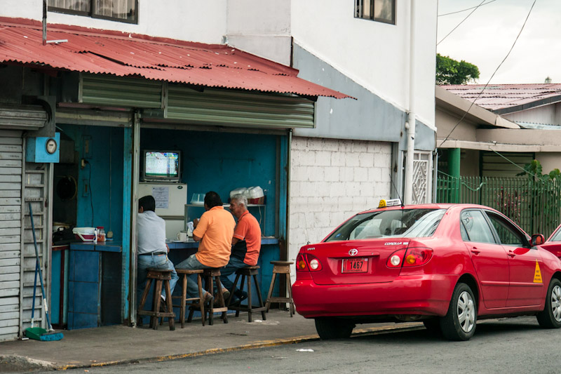 Alajuela. Three men having a snack and watching television.