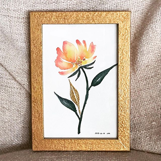 Yellow and orange flower, long stem and three long leaves against a white background. One of the leaves and the inside of the flower are painted with gold. The artwork is framed and I painted the frame in textured gold as well.