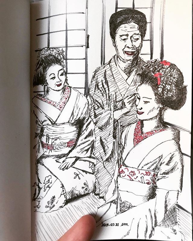 Black and red ballpoint pen drawing of three Japanese women kneeling and smiling. The elderly one is wearing a simple and darker yukata and is applying make up to one of the two younger women. Both are wearing light and elaborate kimonos and their hair is done.