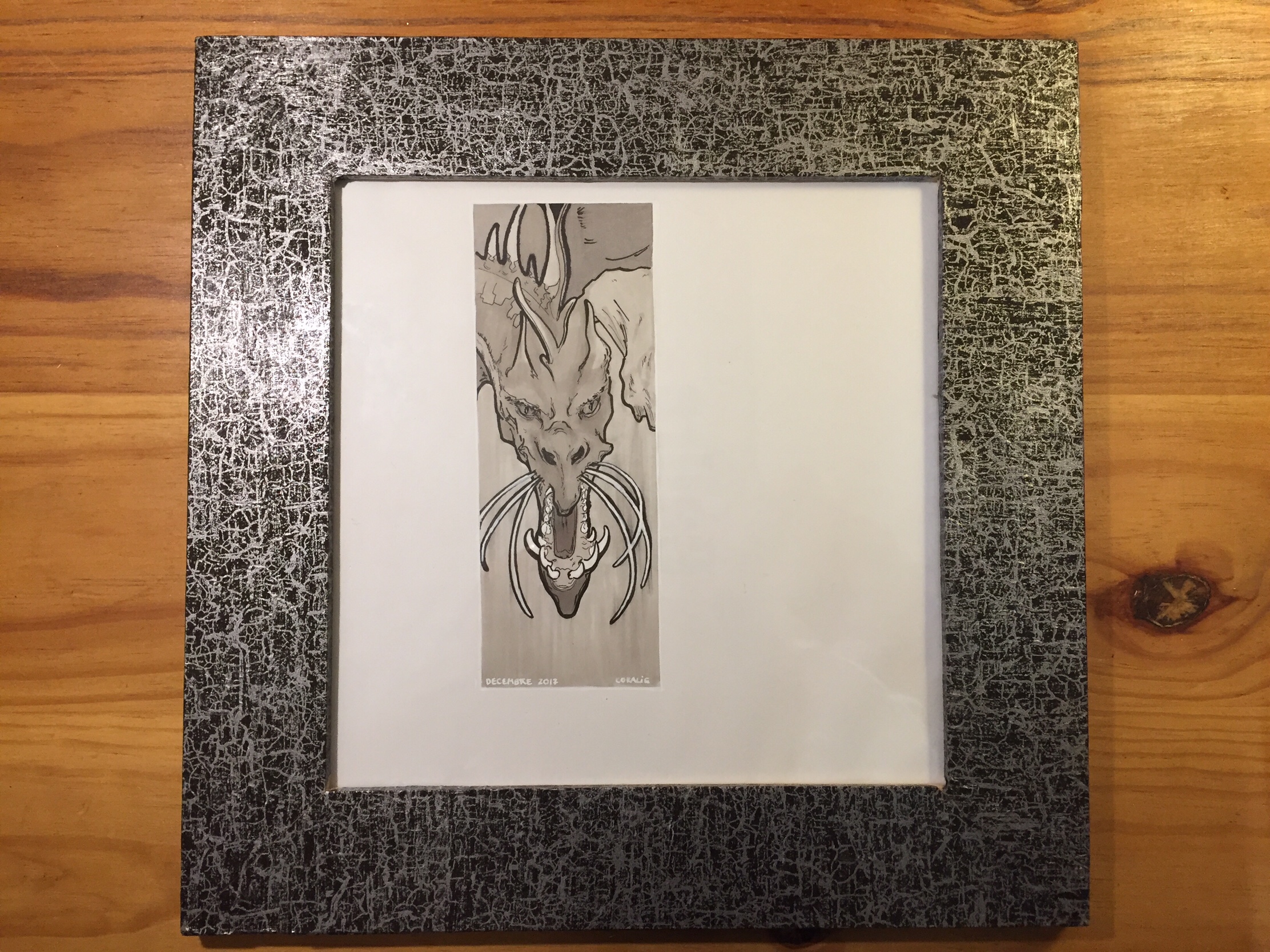 The finished piece: the dragon occupies the left half of a square white sheet of paper. The square frame is adorned with silver and black metallic paper.