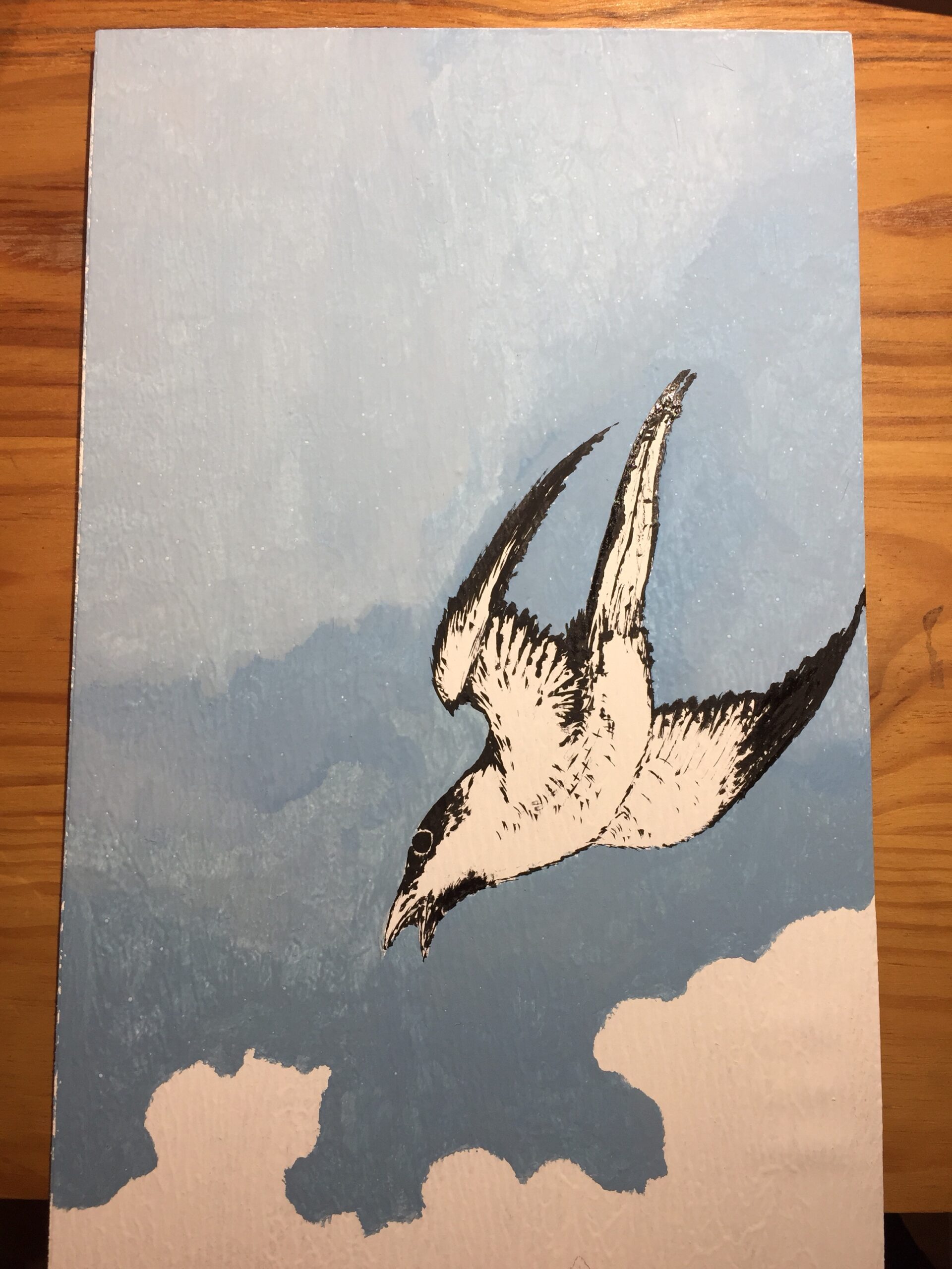 Photo of the part of the board that shows the cuckoo flying downwards which I painted black, and the sky painted in shades of blue over white clouds