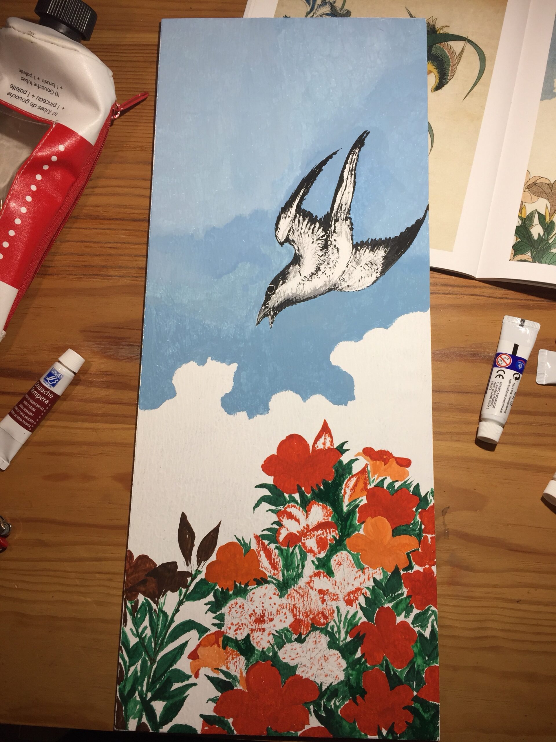 Board with both bird and azalea bush painted. Paint tubes are visible on the wooden table.