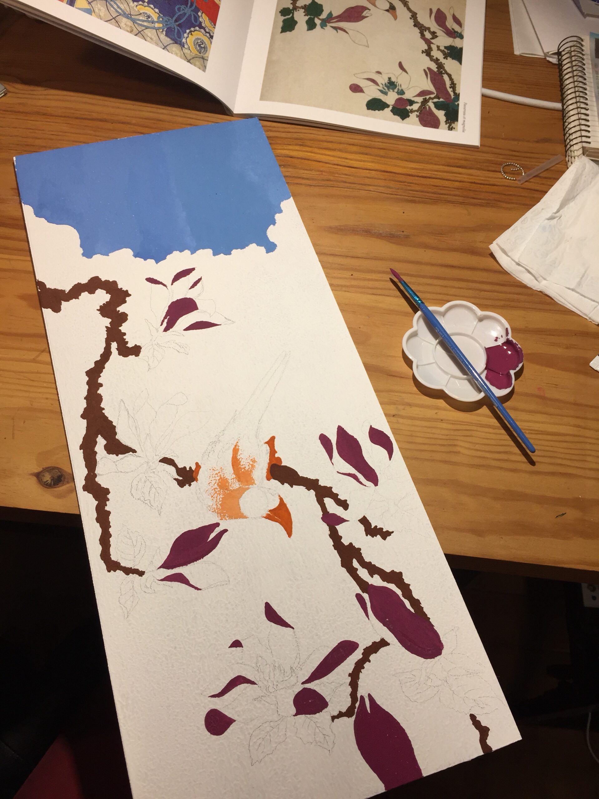 Purple and red gouache paint for the dark petals of the magnolia blossoms. Next to the board is the palette with the paint and the brush I'm using is resting on it.