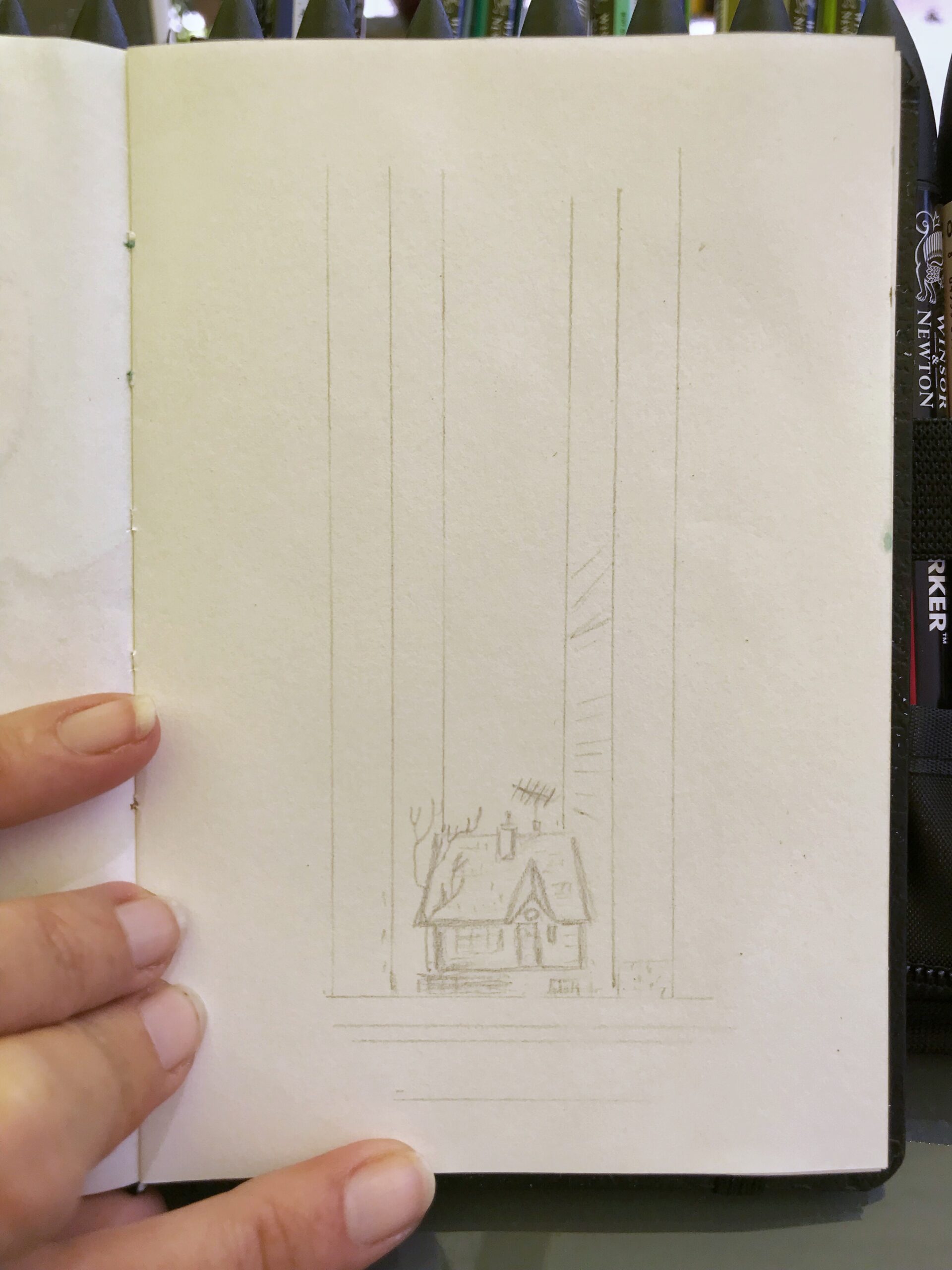 Pencil sketch in an open artbook on a table. My fingers holding the page open are visible.