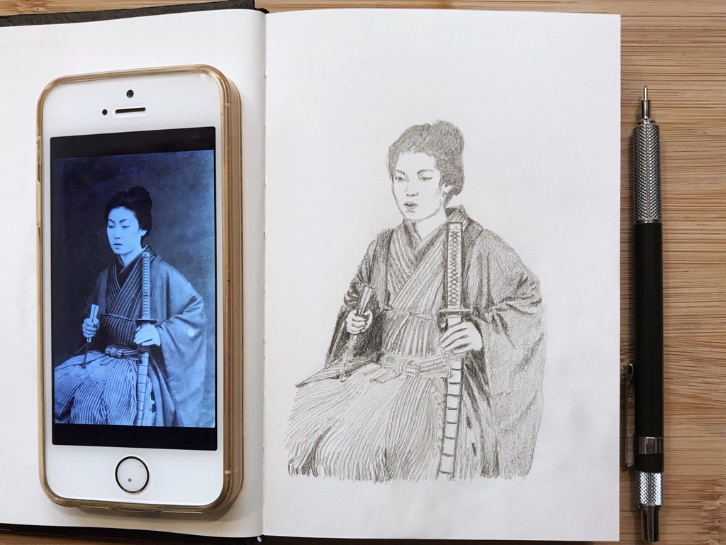 Very detailed pencil drawing of a seated Onna Bugeisha (female warrior) who carries a fan in her right hand and rests her left hand on the sheath of a sword. My iphone displaying the reference photo is at the left of my drawing. My mechanical pencil is visible next to the drawing.