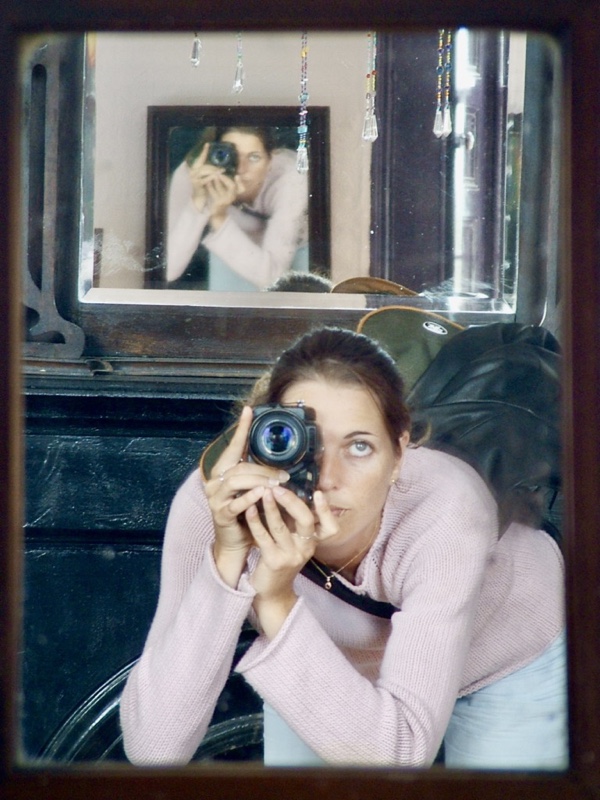 Photo of me, young woman, bending forward as I take a photo of me in a mirror, aiming at a mirror that is reflected in the mirror. My hair is tied in a poney tail. I wear a pink pullover and light blue jeans.
