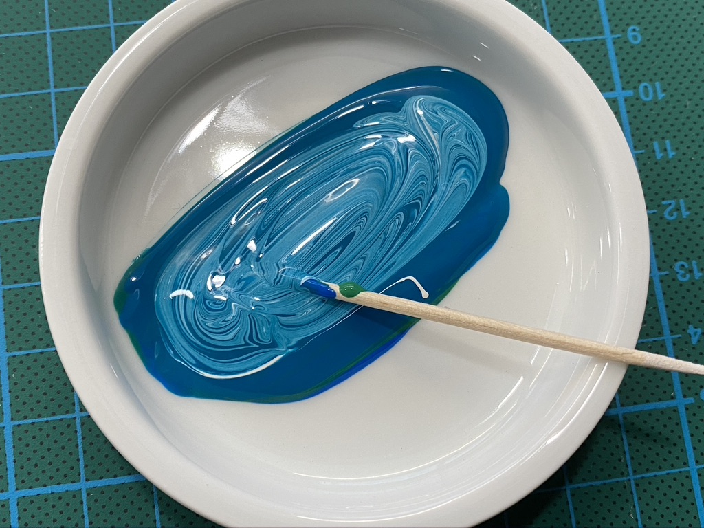 Mixing blue and white gouache paint in a ceramic pan with a toothpick