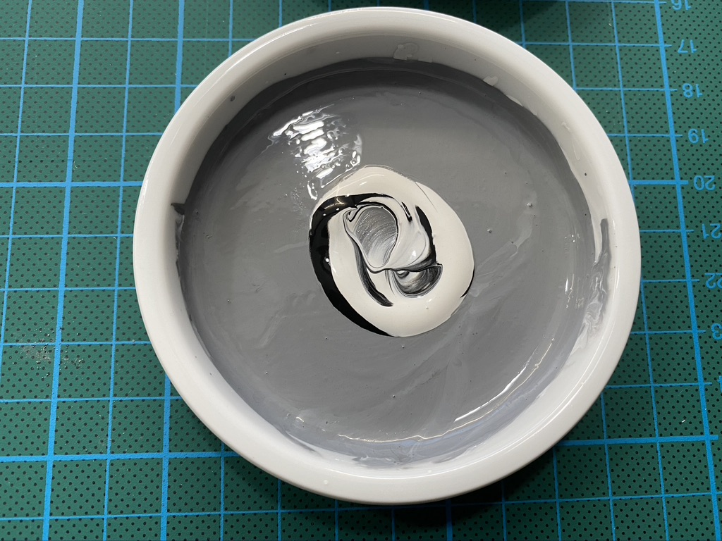 Mixing black and white gouache paint in a ceramic pan