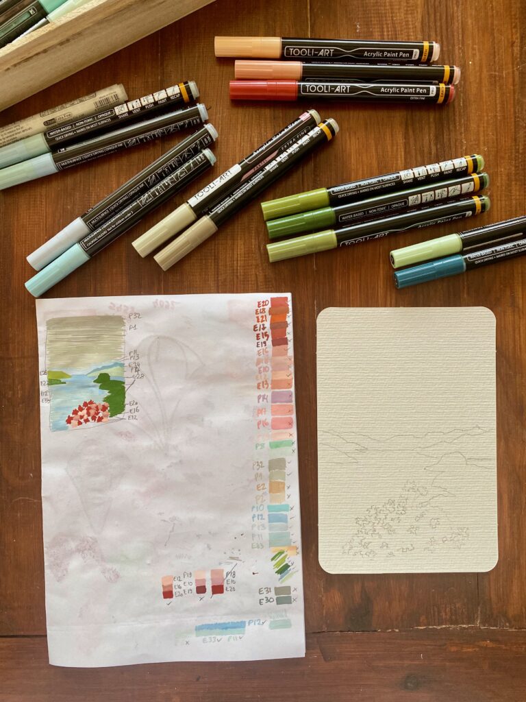 Preparatory sketch on a sheet of regular printing paper where I tried out many of my paint markers which are scattered around the pages on the wooden table.