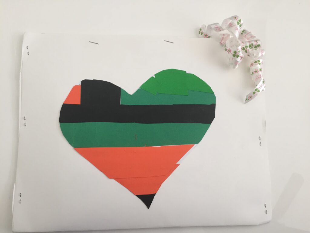 Hand-made envelope of a stapled white folded sheet on which colourful patches form a heart.