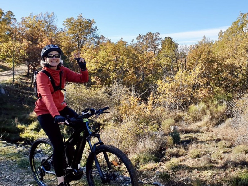 Photo of me riding my electric mountain bike and doing a peace sign on a sunny day. The trees around are turning yellow and orange. I'm wearing a red pullover.