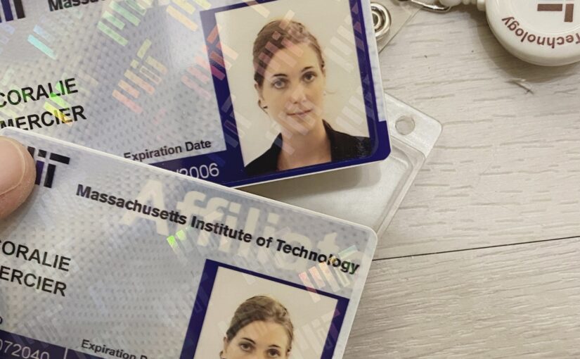 Two Massachusetts Institute of Technology (MIT) identification cards on a wooden surface, with a retractable key holder. The cards show the same individual's photo and name with different expiration dates.