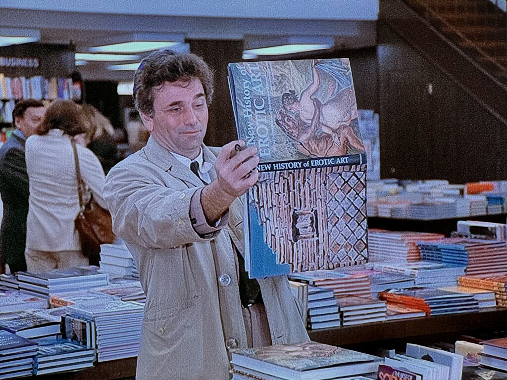In a library, Lieutenant Columbo is holding an open book sideways and at arm’s length, looking perplexed. The book is “New History of Erotic Art”