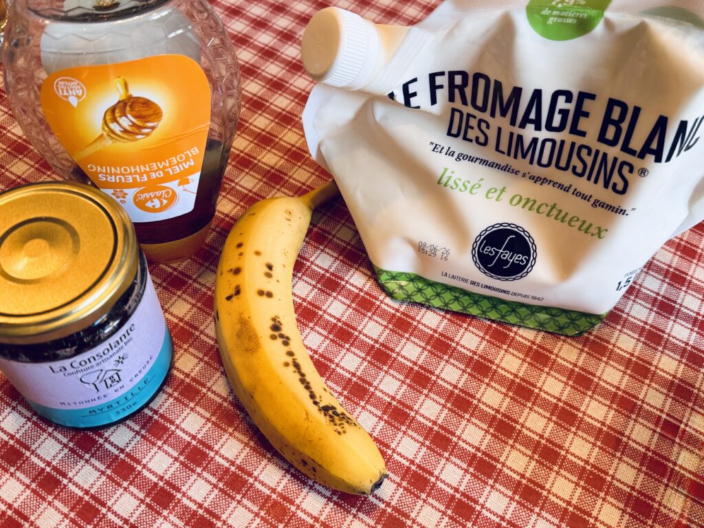 A blueberry preserve jar, a bottle of honey, a banana and a pouch of cottage cheese